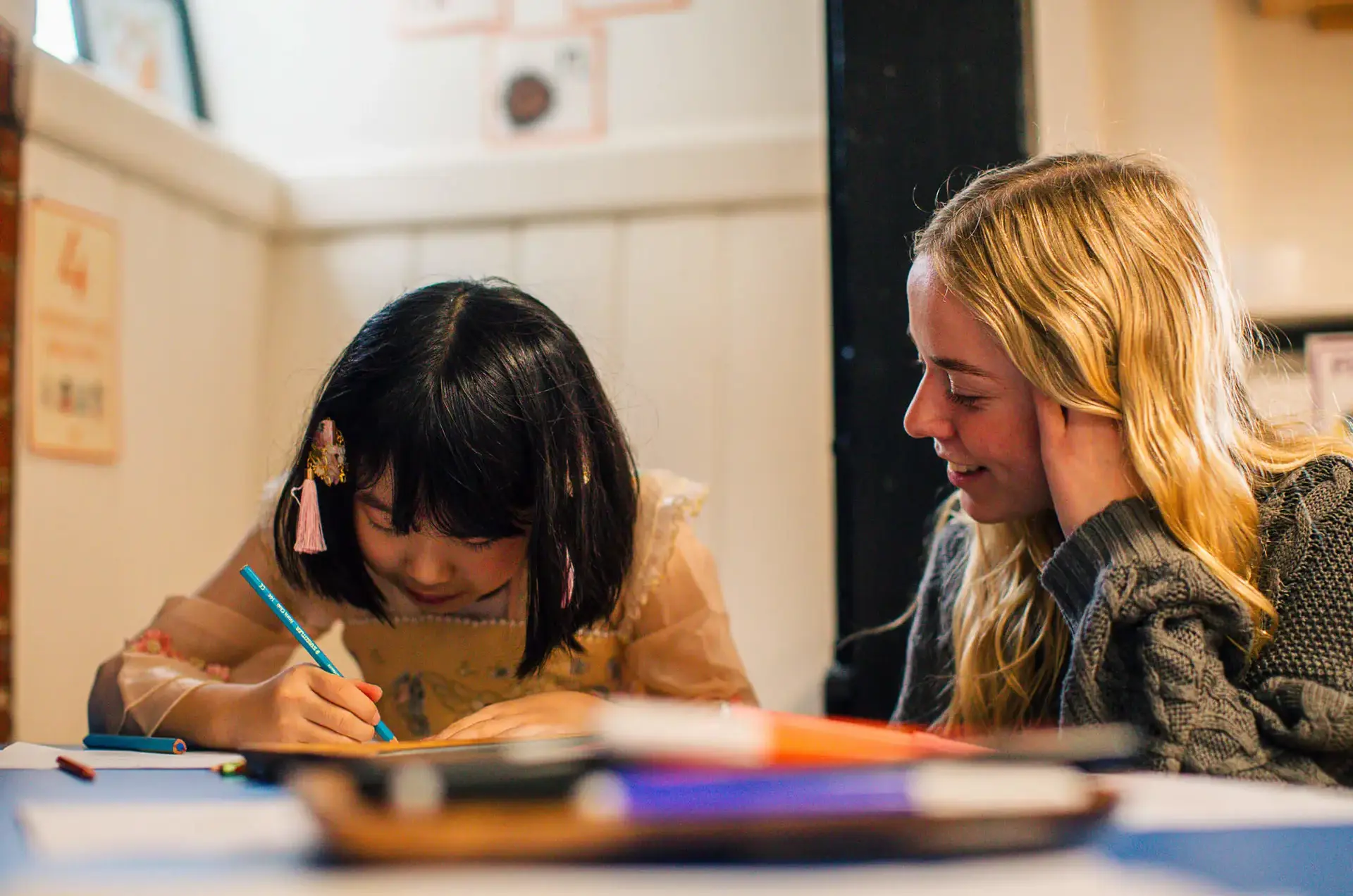 St Chris Junior School pupil writing in her book in class with  her teacher